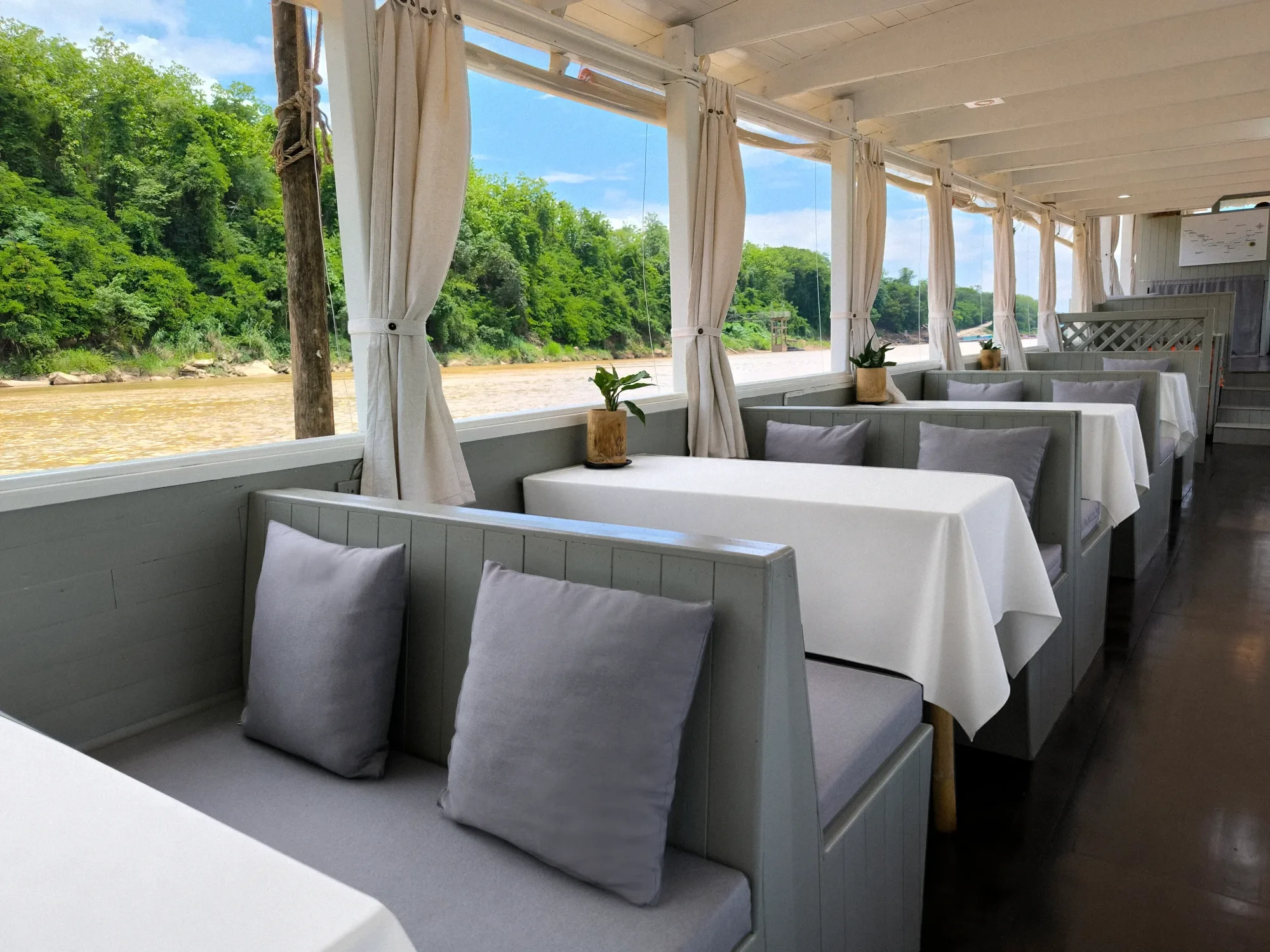 Banquettes à coussins et tables nappées de blanc le long du pont d\x27un bateau Mekong Cruises