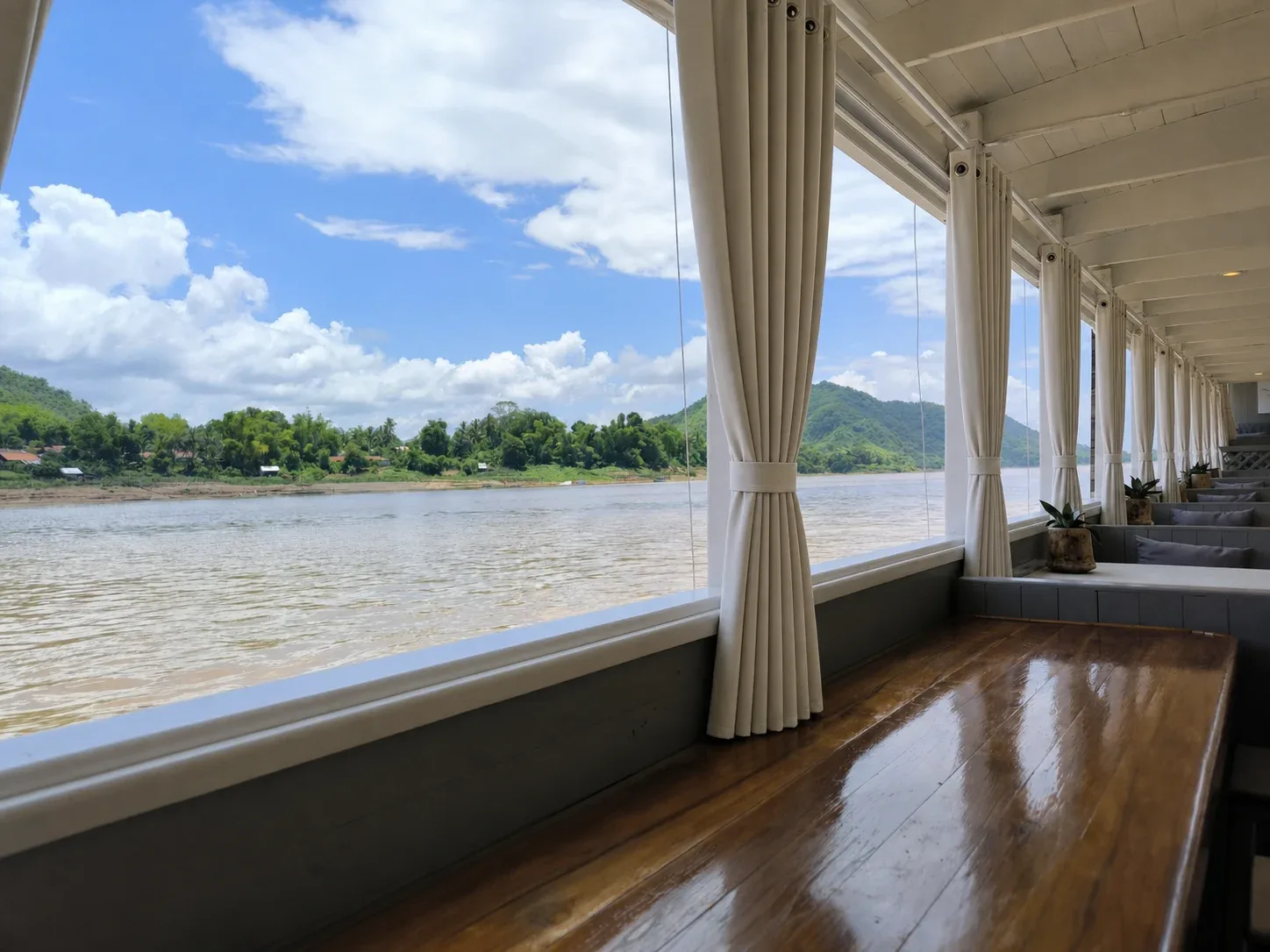 The open deck of the Mekong Cruises boat, curtains tied back, looking out over the river