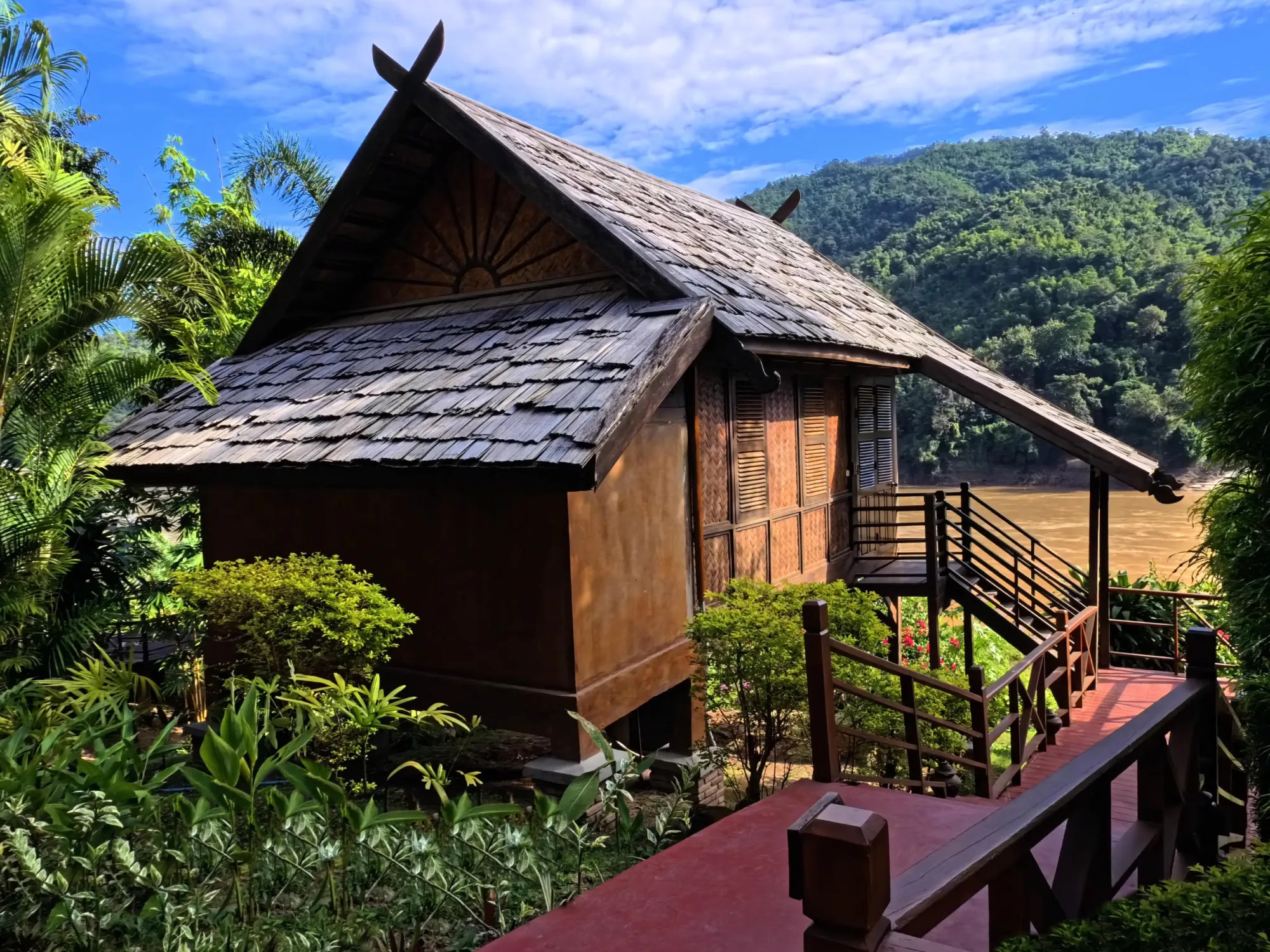 Bungalow au toit pointu en bardeaux et balustrade en bois surplombant le Mékong