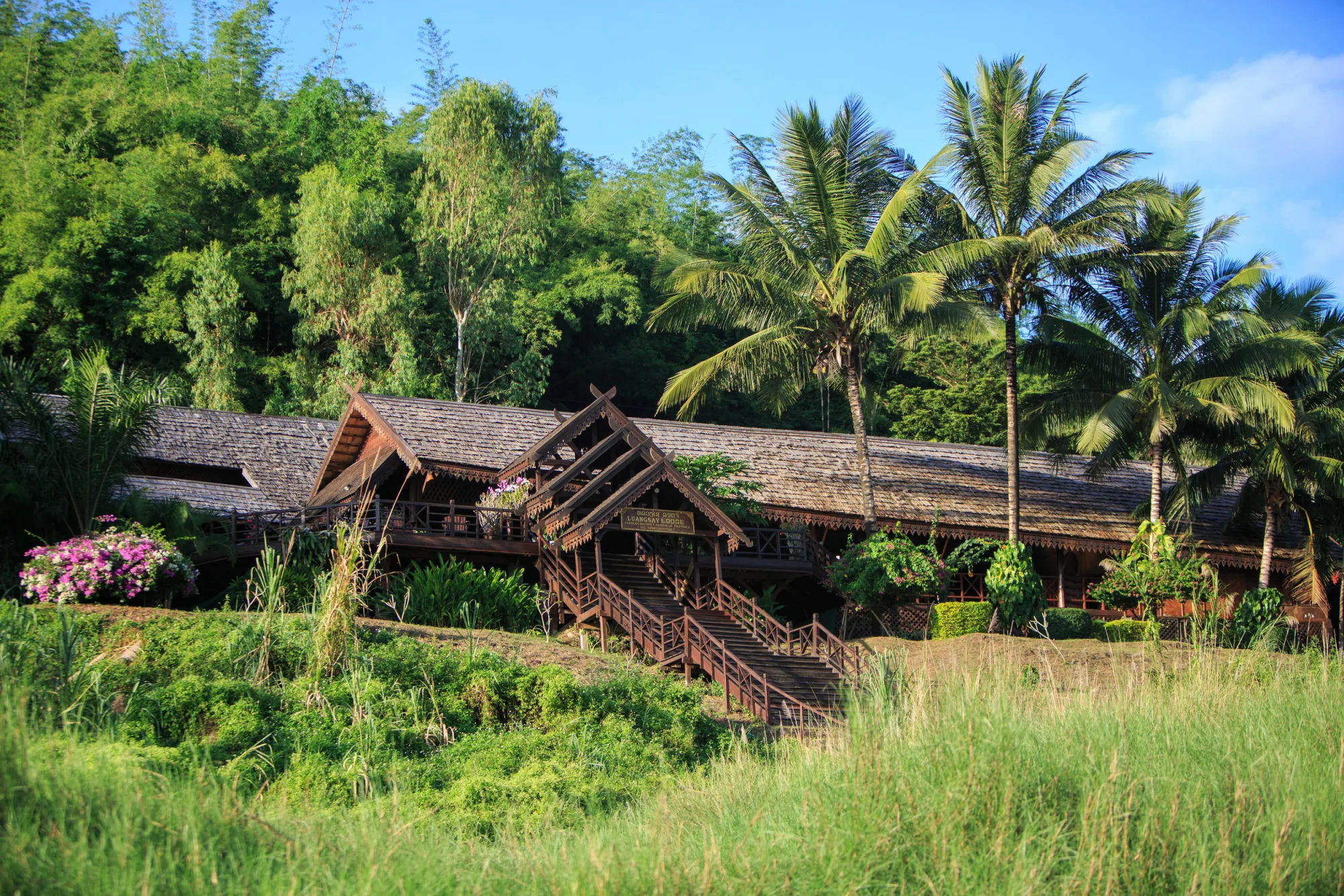 The teak-and-rosewood roofline of Luang Say Lodge among palms above the Mekong